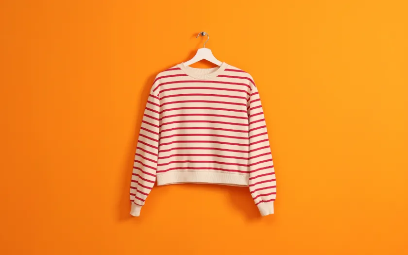 Imagem de uma camisola branca com riscas pendurada num cabide, sob fundo cor de laranja. Crédito: Shutterstock.