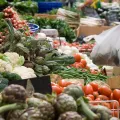 Imagem de mulher a comprar vegetais numa praça. Crédito: Canva