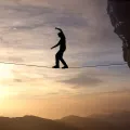 Imagem de um homem a caminhar numa arame suspenso entre duas rochas. Crédito: Canva