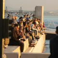Pessoas de várias idades estão sentadas junto ao rio tejo, em Lisboa, ao entardecer. Crédito: Shutterstock