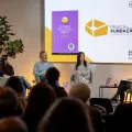Quatro pessoas sentadas no palco, com uma plateia a assistir, e um ecrã que tem a capa de um livro da Fundação.