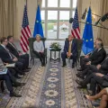 Ursula von der Leyen sentada ao lado de Donald Trump, com bandeiras da UE e dos EUA.