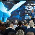 Uma plateia de costas a assistir à apresentação de duas mulheres, num palco. Texto "Europe's Energy Transition".