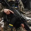 Um soldado carrega uma arma ao peito, com a bandeira ucraniana destacada no seu colete de proteção. Créditos: shutterstock