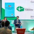 Imagem de quatro pessoas a conversar perante uma plateia,  sob um fundo verde.