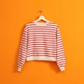 Imagem de uma camisola branca com riscas pendurada num cabide, sob fundo cor de laranja. Crédito: Shutterstock.