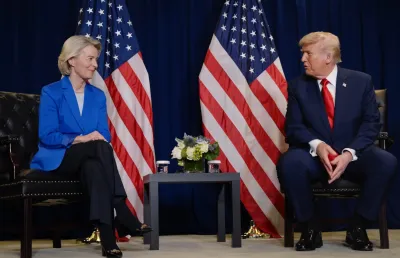 Ursula von der Leyen sentada ao lado de Donald Trump, com duas bandeiras dos EUA atrás.