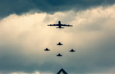 Um avião comercial em pleno voo escoltado por vários caças sob um céu enevoado. Crédito: Canva