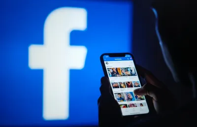 Imagem de uma pessoa, de costas, com um telemóvel na mão a usar o Facebook. Crédito: Shutterstock.