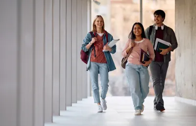 Imagem de três jovens a caminhar pelos corredores de uma universidade. Crédito: Shuterstock
