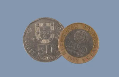 Duas moedas de escudo, de cinquenta escudos e de duzentos escudos, sob fundo neutro. Crédito: Canva