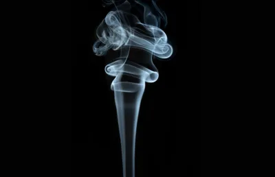 Fumo de um cigarro ergue-se no ar sob fundo negro. Crédito : Shutterstock.