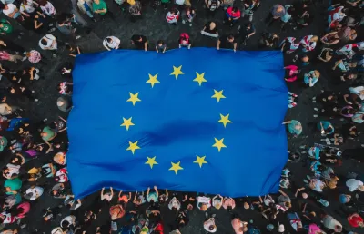 VIsta de cima de dezenas de pessoas carregam uma bandeira azul muito grande da União Europeia. Crédito Canva