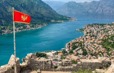 Vista de um rio e de uma cidade  rodeada de montanhas onde se ergue uma bandeira  do Montenegro. Crédito: Canva