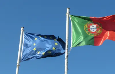 Imagem de bandeiras asteadas de Portugal e da União Europeia, sob um fundo azul.