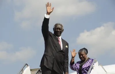 Um homem negro, vestido de fato e gravata, sai de um avião, Presidente do Gana e da Uinão Africana em 2007, John Kufuor. Crédito:  Creative Commons CC0 License