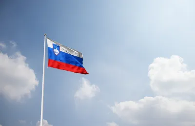 A bandeeira da Eslovénia hasteada, ondulando sob  um céu com nuvens. Crédito: Shutterstock.