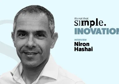 A black-and-white close-up portrait of Niron Hashai, with a light blue background and the text “It’s not that simple. An interview on innovation.”