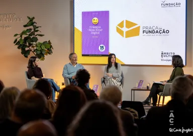 Quatro pessoas sentadas no palco, com uma plateia a assistir, e um ecrã que tem a capa de um livro da Fundação.