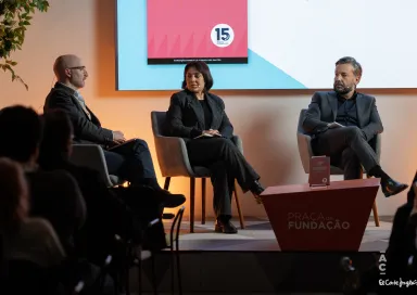 Dois homens e uma mulher sentados, em palco, à conversa sobre o livro da Fundação, que está pousado numa mesa entre eles