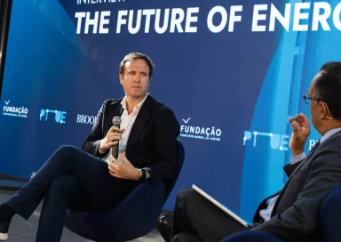 O jornalista britânico Ed Conway em palco, sentado, com um microfone na mão. O entrevistador de costas. Fundo azul com o texto "The Future of Energy". DR/FFMS