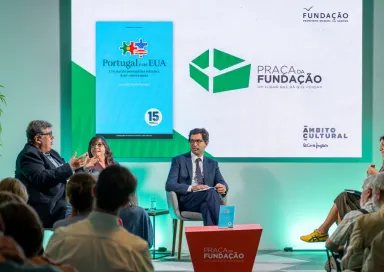 Imagem de quatro pessoas a conversar perante uma plateia,  sob um fundo verde.