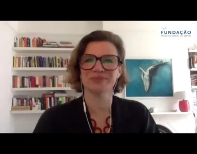 A economista Mariana Mazzucato sobre um fundo com estantes de livros e um quadro de uma baleia.