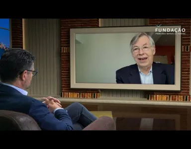 O jornalista Pedro Pinto, num estúdio de televisão, a olhar para uma tela que mostra François Heisbourg a falar.
