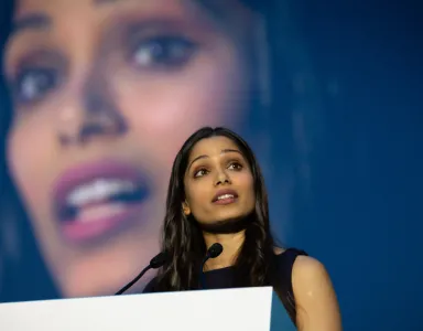 Freida Pinto num púlpito a discursar, com uma imagem da própria atriz no fundo.