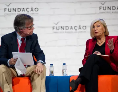 Dois palestrantes numa mesa redonda. Fundo com a palavra "FUNDAÇÃO" repetida.