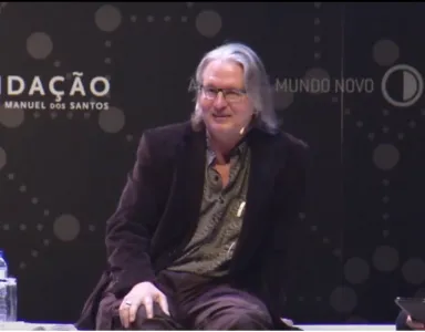 Bruce Sterling a falar, no palco da Casa da Música do Porto, sobre um fundo com o logo da Fundação Francisco Manuel dos Santos.