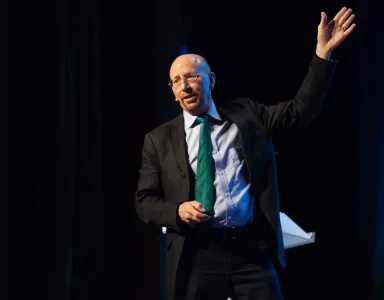 Richard Baldwin a discursar, com uma mão levantada, sobre um fundo escuro, ligeiramente iluminado. 