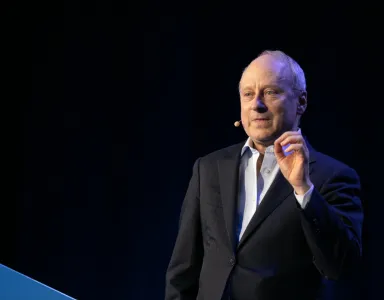 O filósofo Michael Sandel a falar, de pé, com um microfone sem fios, sobre um fundo preto. 