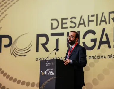 Homem fala num púlpito, ao fundo o texto "DESAFIAR PORTUGAL - OPORTUNIDADES DA PRÓXIMA DÉCADA".