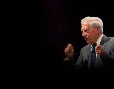 Mario Vargas Llosa a discursar. Fundo escuro.