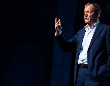 Alastair Campbell em palco, gesticulando enquanto fala ao microfone.