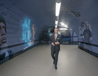 O jornalista Carlos Daniel a andar num túnel com murais de rostos e texto nas paredes.