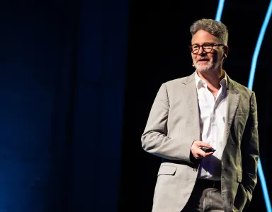 O historiador Adam Tooze a falar numa conferência, com um comando na mão, sobre um fundo escuro-