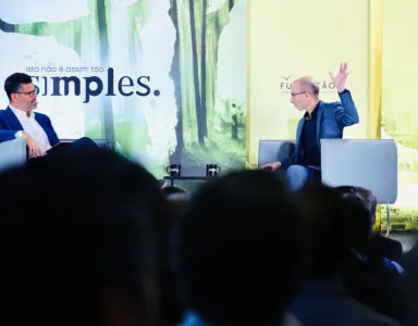 Harari e o jornalista Pedro Pinto conversam num evento ao vivo; um levanta a mão. Texto: "isto não é assim tão simples."
