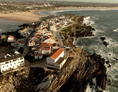 Vista aérea de uma aldeia costeira com casas de telhados laranja junto ao mar.
