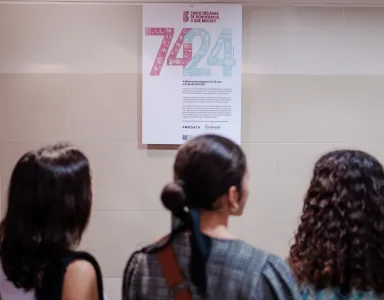 Três raparigas estudantes a ver um cartaz que tens os números "74" e "24" em destaque.