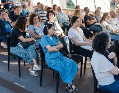 Plateia a assistir a um evento ao ar livre, sobre mulheres refugiadas em Portugal.