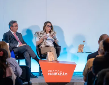 Quatro pessoas em debate, num palco, com o texto "PRACA da FUNDAÇÃO" em destaque.