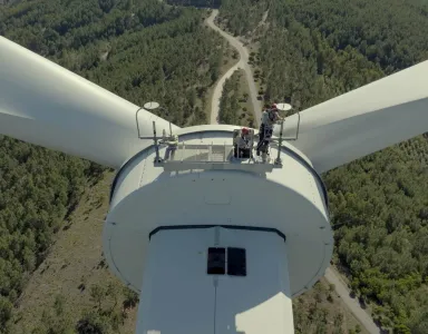 Vista de cima de uma turbina eólica, com duas pessoas na plataforma de manutenção.