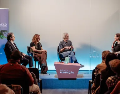 Quatro pessoas em destaque num painel, com o texto "PRAÇA da FUNDAÇÃO" em primeiro plano.