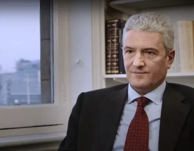 Homem com cabelo grisalho, no caso o professor Francisco Bethencourt, sentado em frente a uma janela, com prateleira de livros atrás.