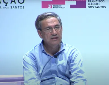 Orhan Pamuk sentado num banco. Fundo branco com o logotipo da Fundação.