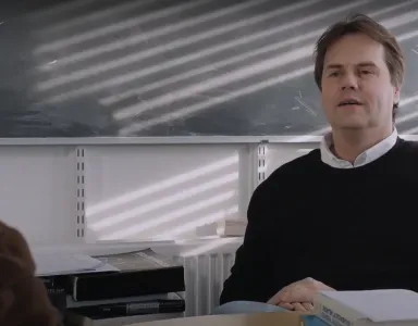 O astrofísico Pedro Ferreira sentado, numa sala de aula. Ao fundo, reflexos de luz no quadro.