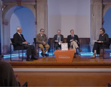 Imagem de um painel com cinco pessoas sentadas em cadeiras, com o texto "Fundação" visível numa mesa laranja que está ao centro.