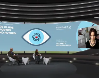 Um homem e uma mulher sentados, num estúdio de televisão, a olhar para uma tela, na qual está Elissa Epel a falar. Do lado oposto da tela lê-se "De olhos postos no futuro". 